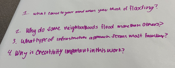 A sheet of paper shows four handwritten discussion questions in purple marker about flooding, infrastructure, and creativity.